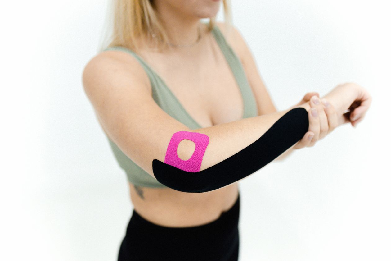 woman applying kinesio tape on her arm for therapeutic treatment of elbow tendinopathy and overuse injury