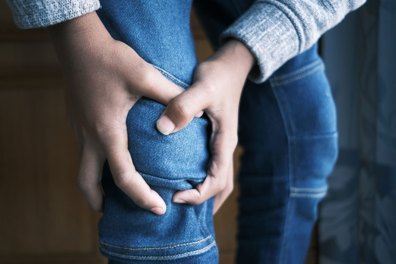 hands holding knee through jeans showing joint pain and arthritis discomfort