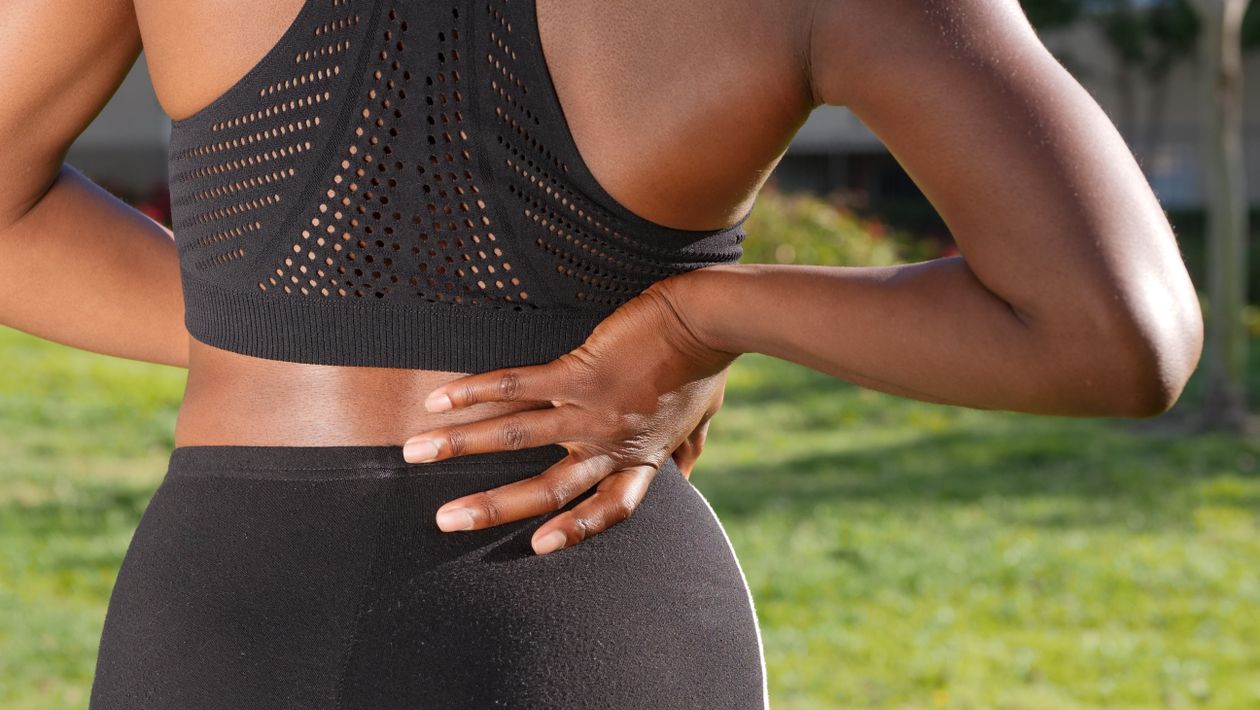 woman in athletic wear holding her lower back after outdoor exercise