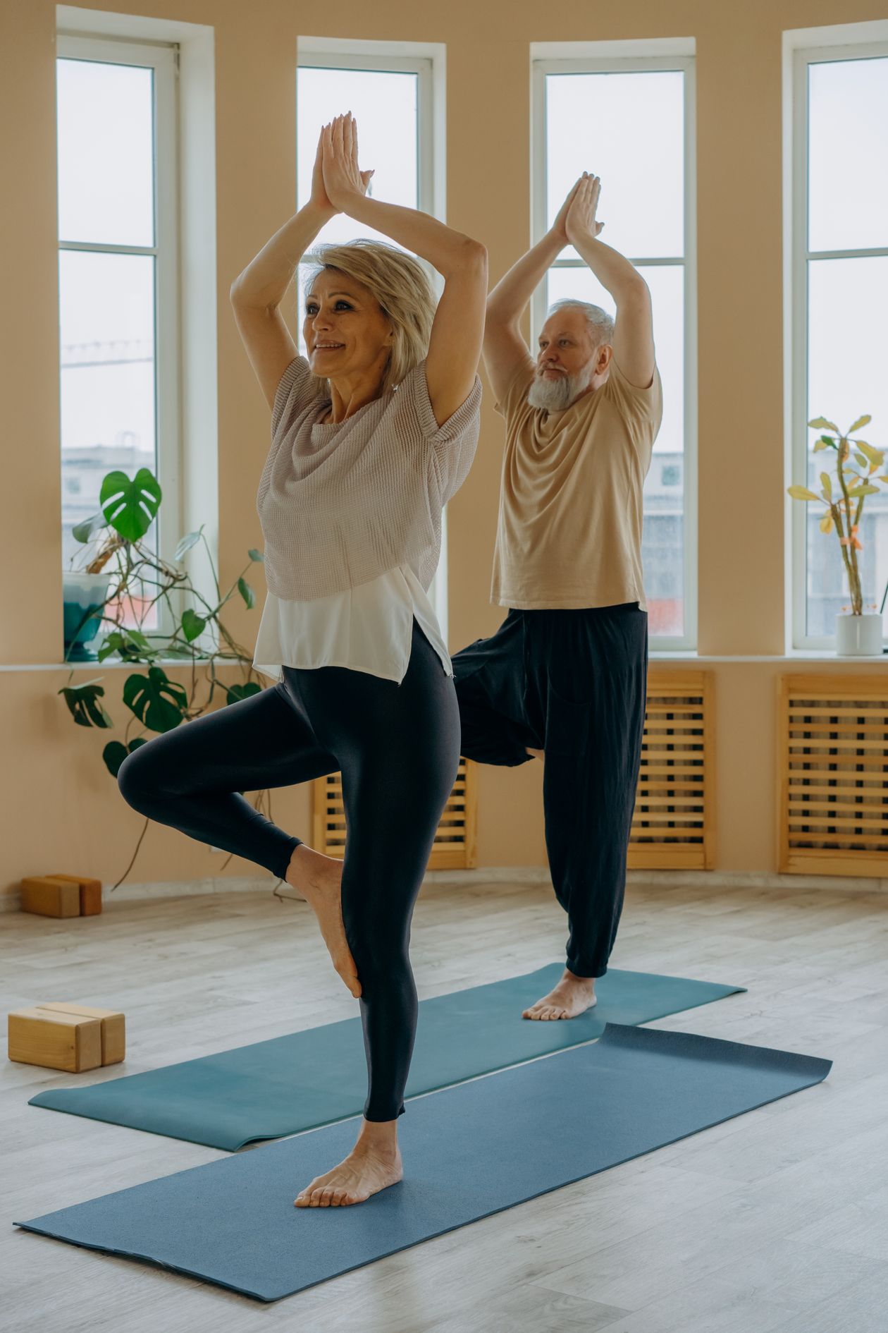 elderly couple performing yoga balance poses on mats indoors promoting wellness and active aging