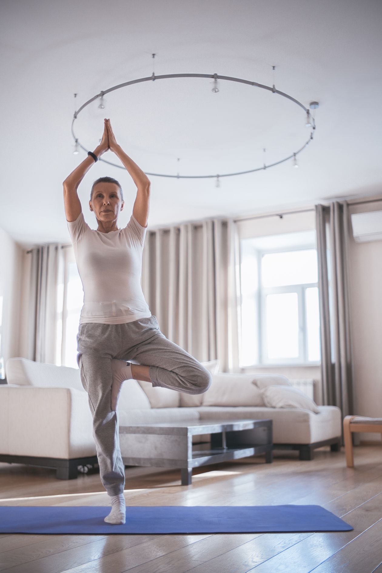 senior woman doing tree pose yoga for balance training indoors in a bright living room