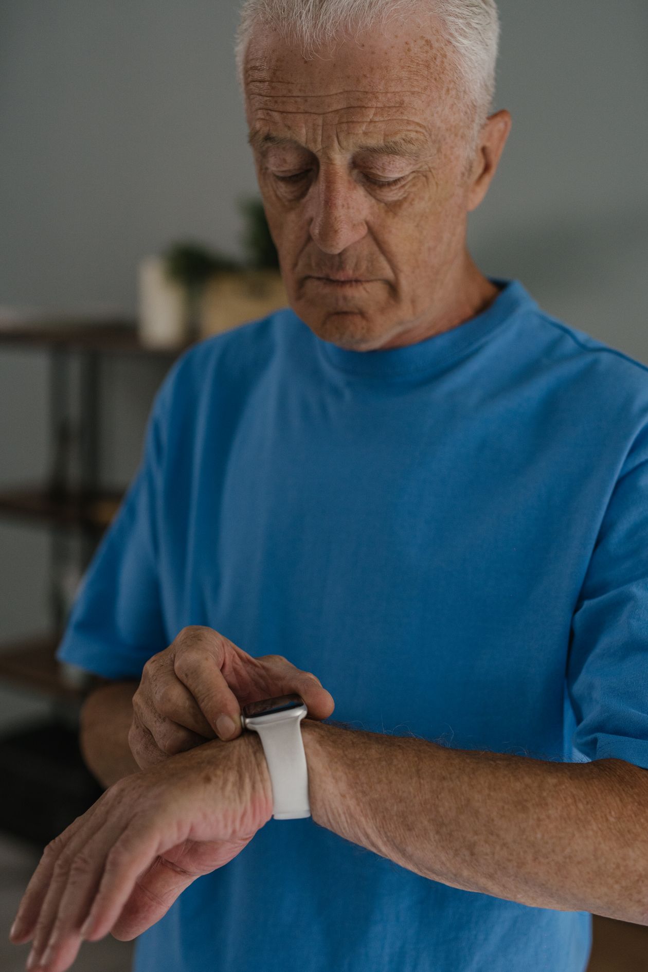 elderly man in blue shirt checking his smartwatch indoors