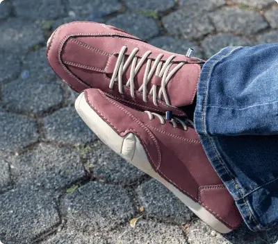 person wearing Grounded Evolve shoes in wine red on cobblestone street showing everyday casual wear and natural foot movement for adults over 40