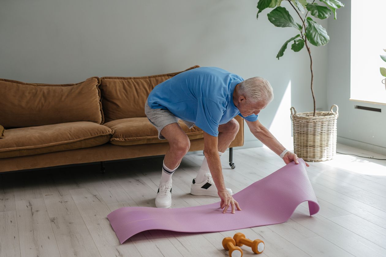 elderly man setting up yoga mat at home for joint-friendly home gym workout