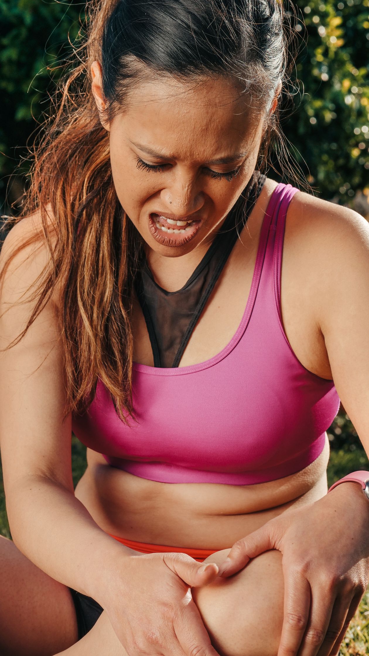 Asian woman in sportswear holding her knee in pain during outdoor exercise showing IT band syndrome symptoms