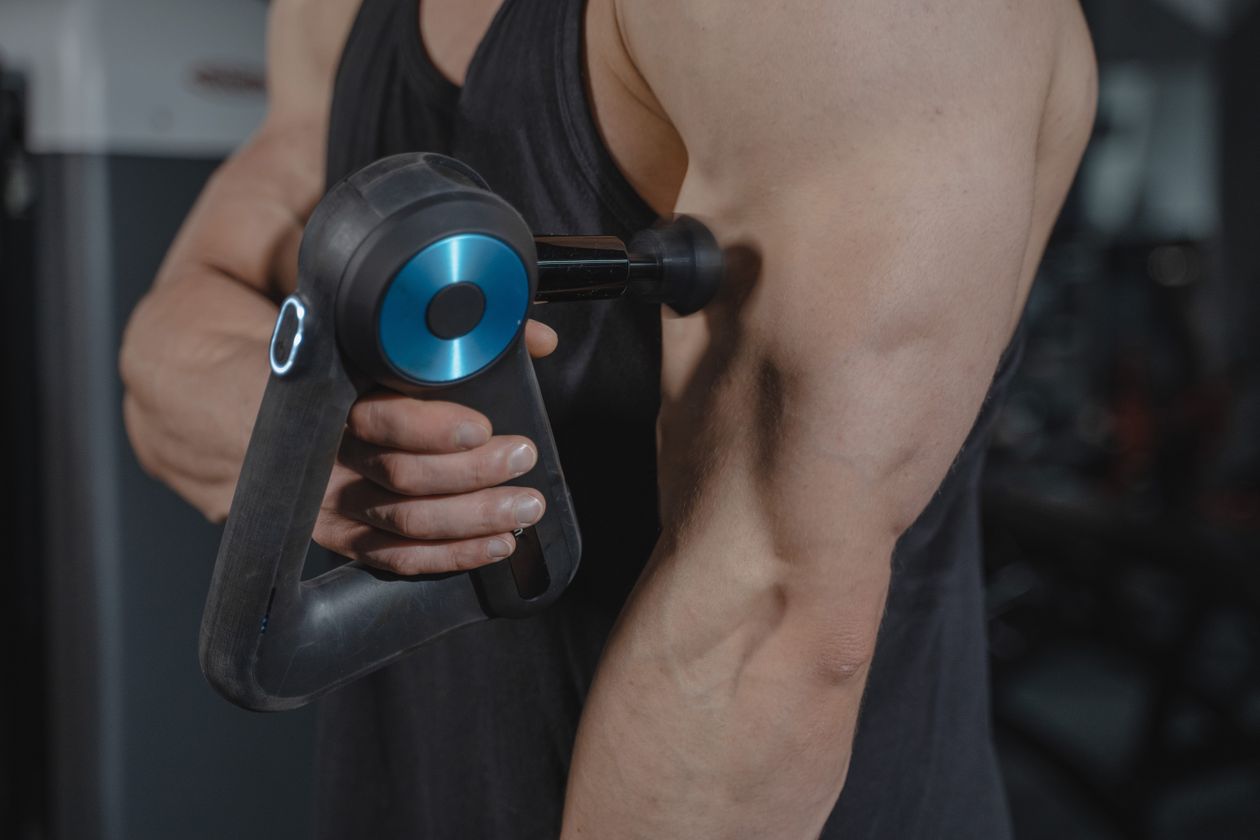 man using a massage gun on his arm for muscle relaxation and recovery showing percussive therapy for adults