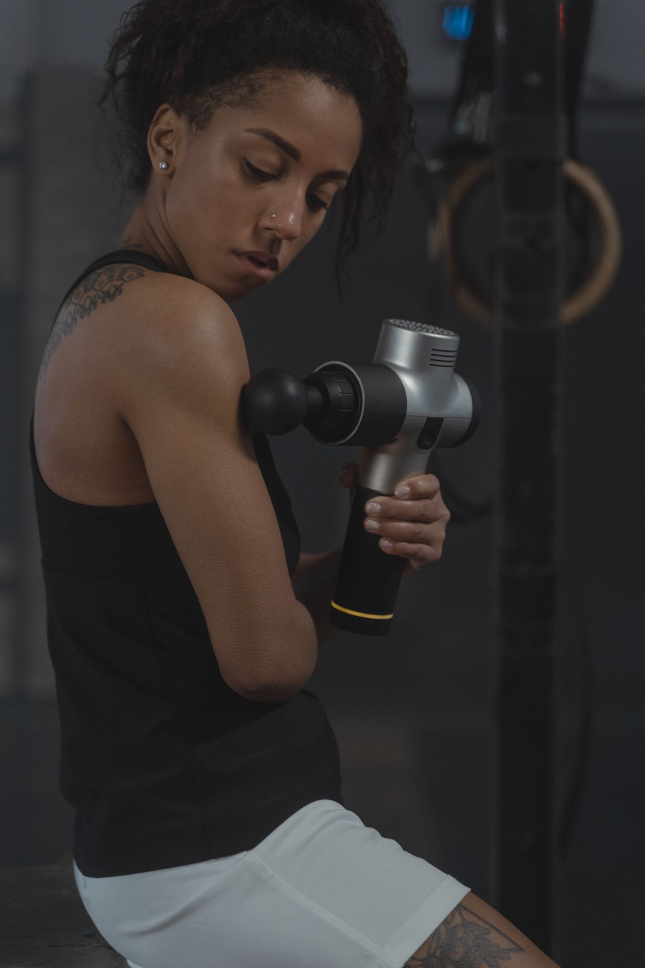 woman using a percussion massager on her arm in a gym for muscle recovery showing correct massage gun technique