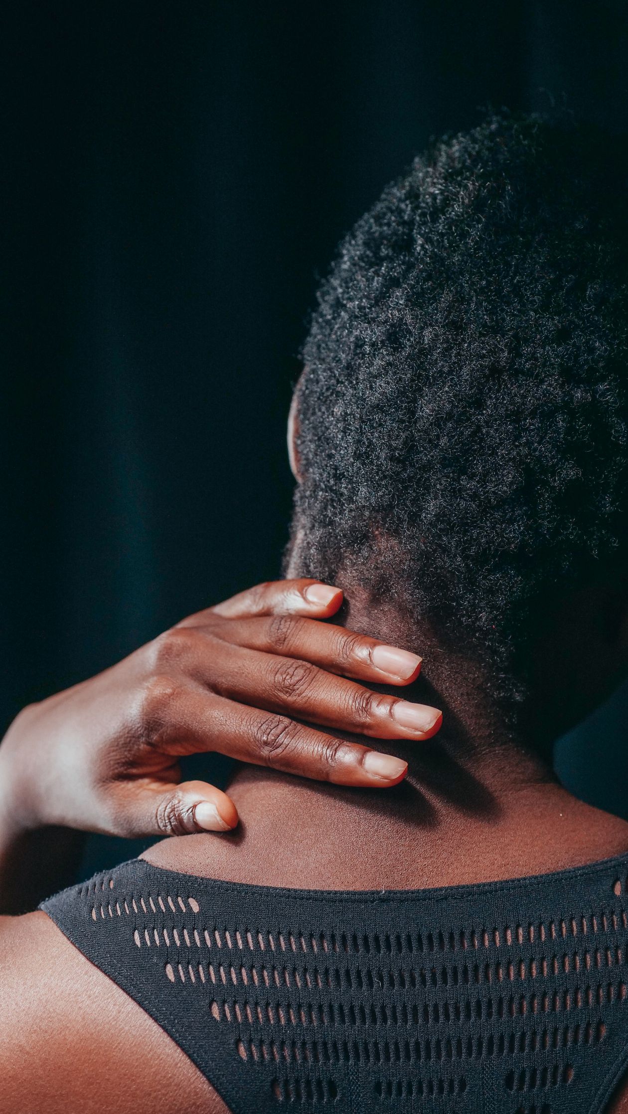 person touching their neck showing cervical discomfort on dark background representing neck pain in adults