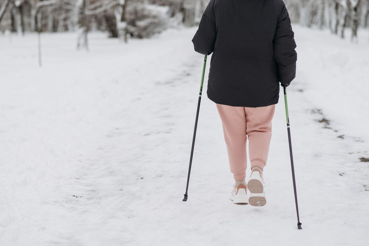 person using trekking poles walking on a snow-covered path in winter
