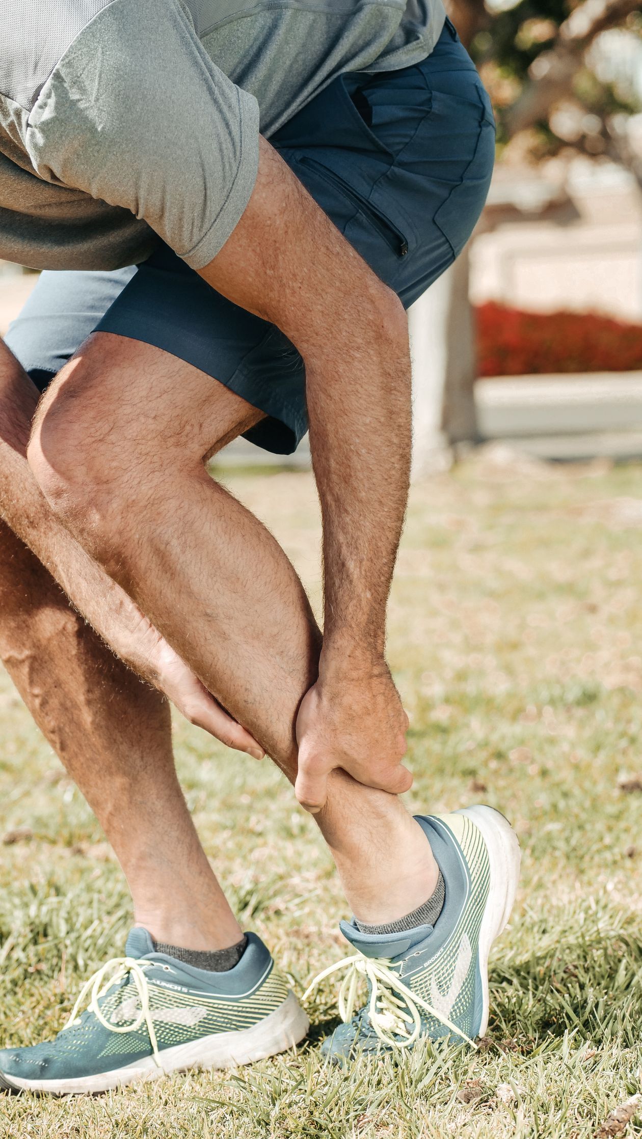 adult holding ankle while wearing running shoes outdoors showing foot and ankle pain