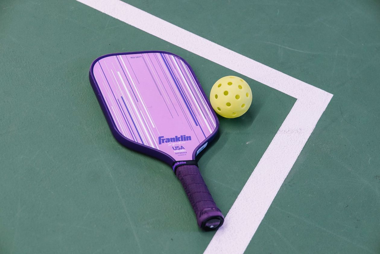 purple pickleball paddle and yellow ball on green court showing pickleball equipment for older adults