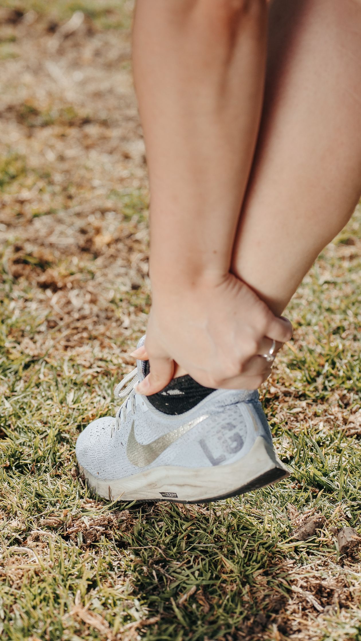 close-up of a person holding their ankle in a sneaker indicating heel or plantar fascia pain