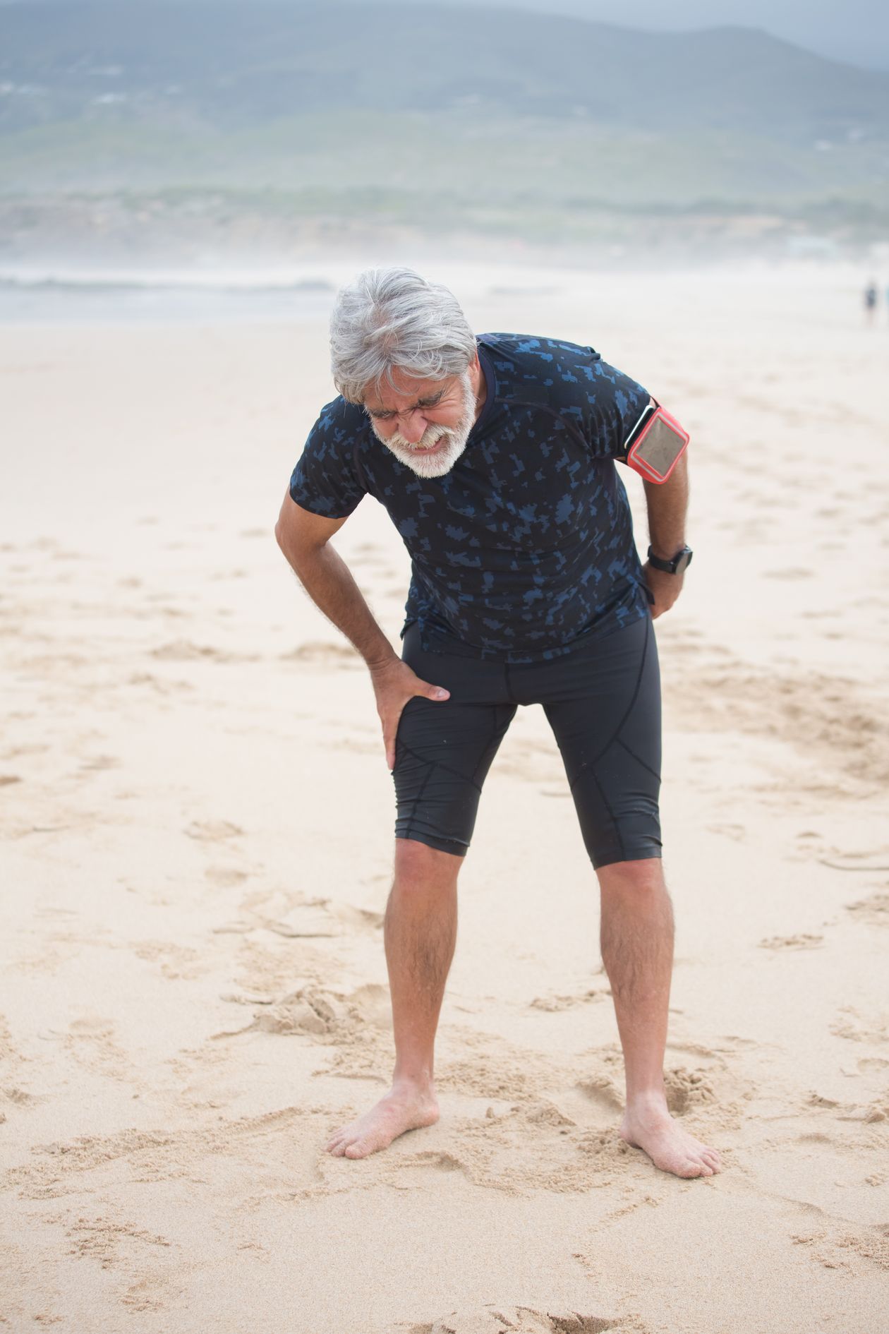elderly man stretching leg on beach showing active aging and knee pain management strategies for adults over 60