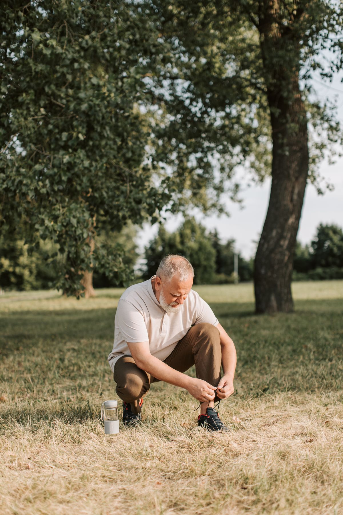 senior man tying shoelaces on grassy field before exercise
