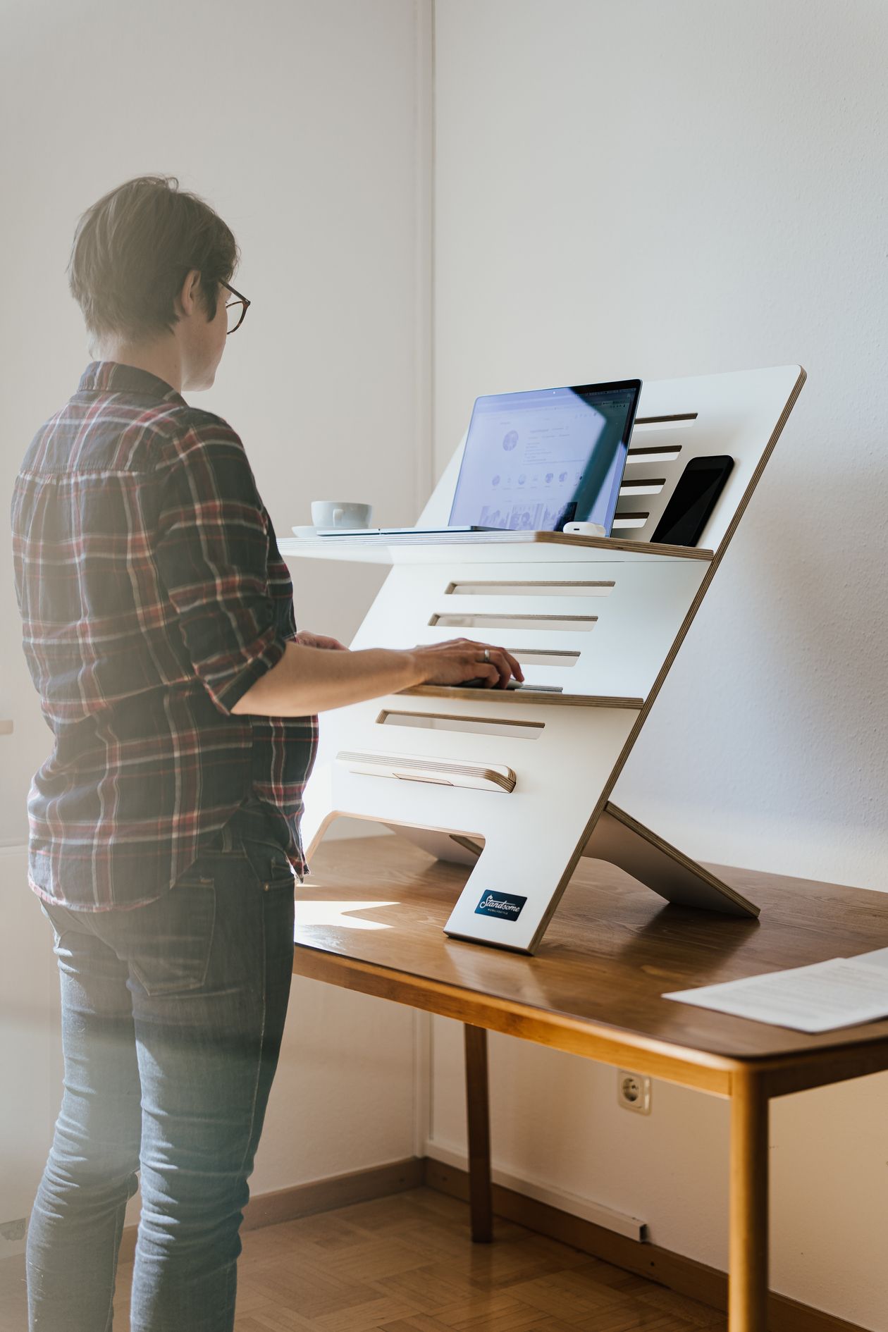 woman working on a laptop at an adjustable standing desk in a home office showing ergonomic workspace setup