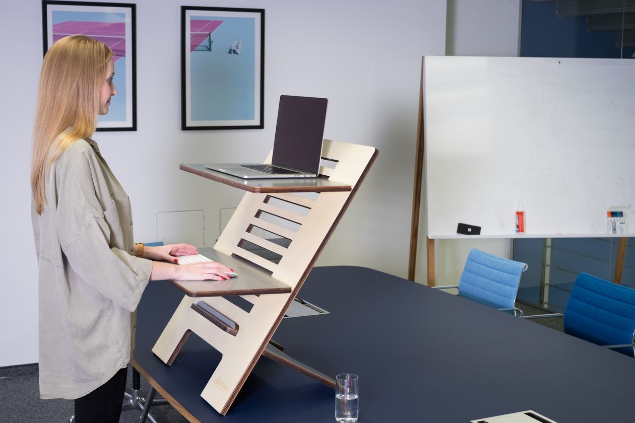 woman using a standing desk with laptop in a modern office setting showing ergonomic workspace for back health