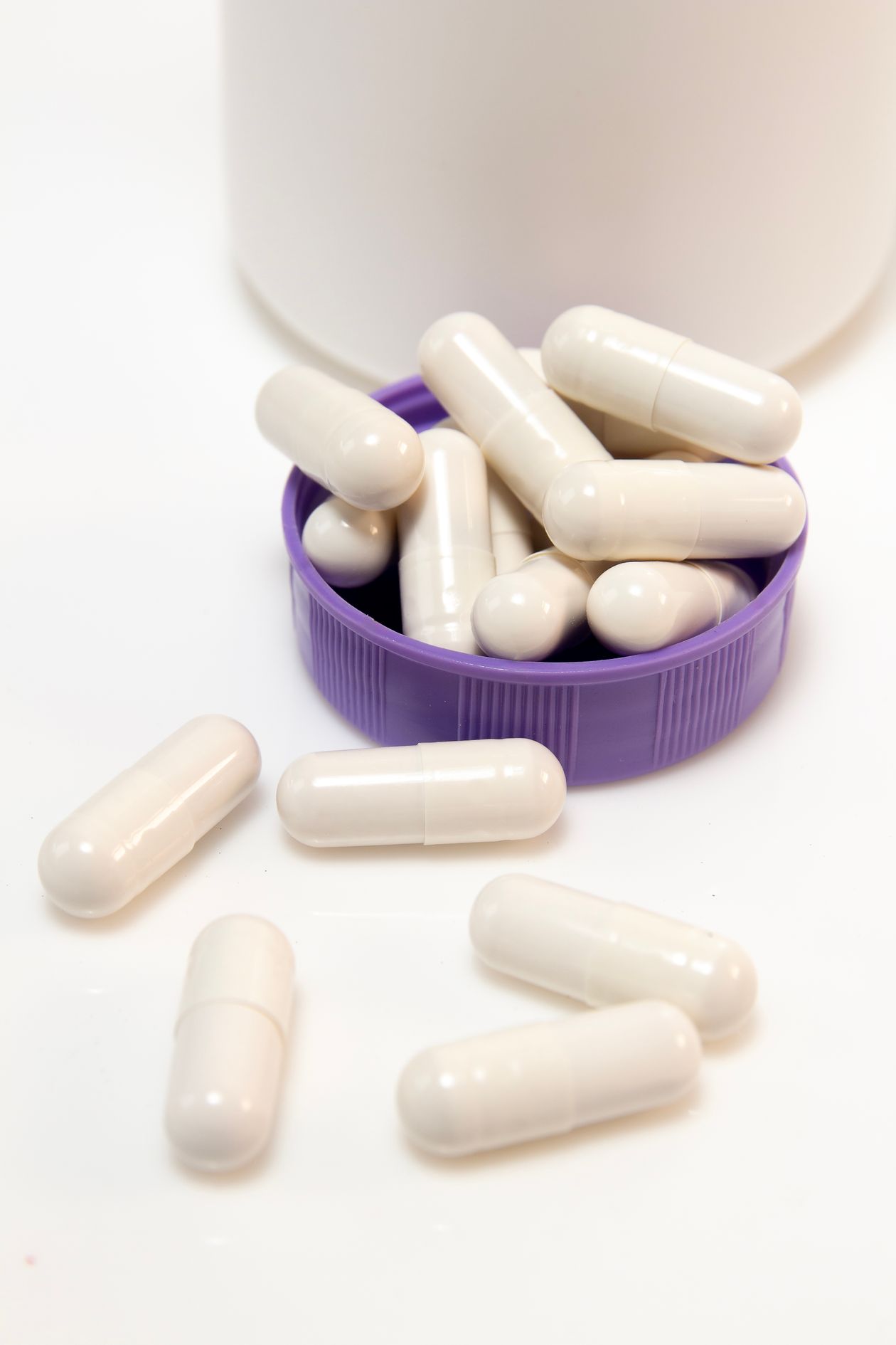 white gel capsules spilling from a supplement container showing oral hyaluronic acid supplement form