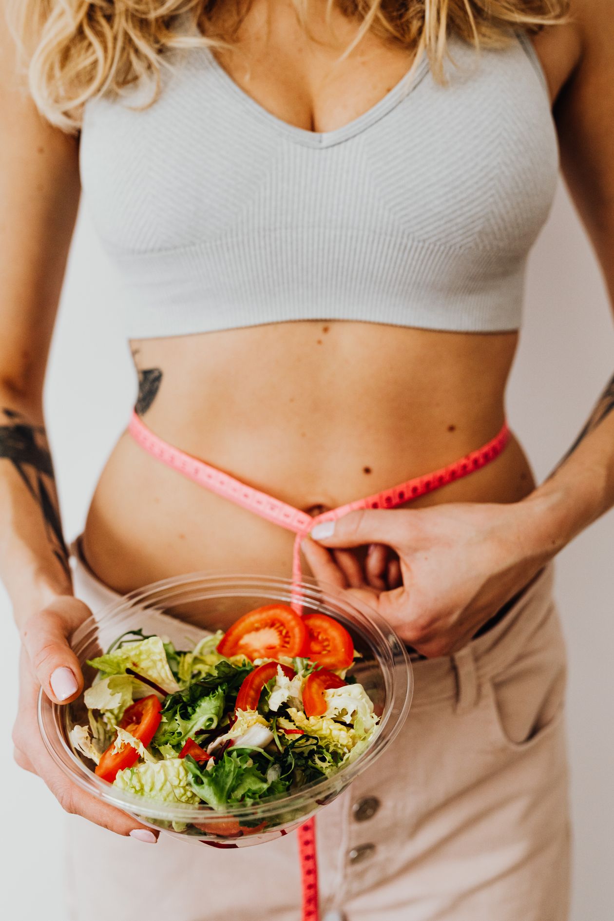 fit woman measuring waist while holding a salad bowl showing healthy diet and weight management for joint health