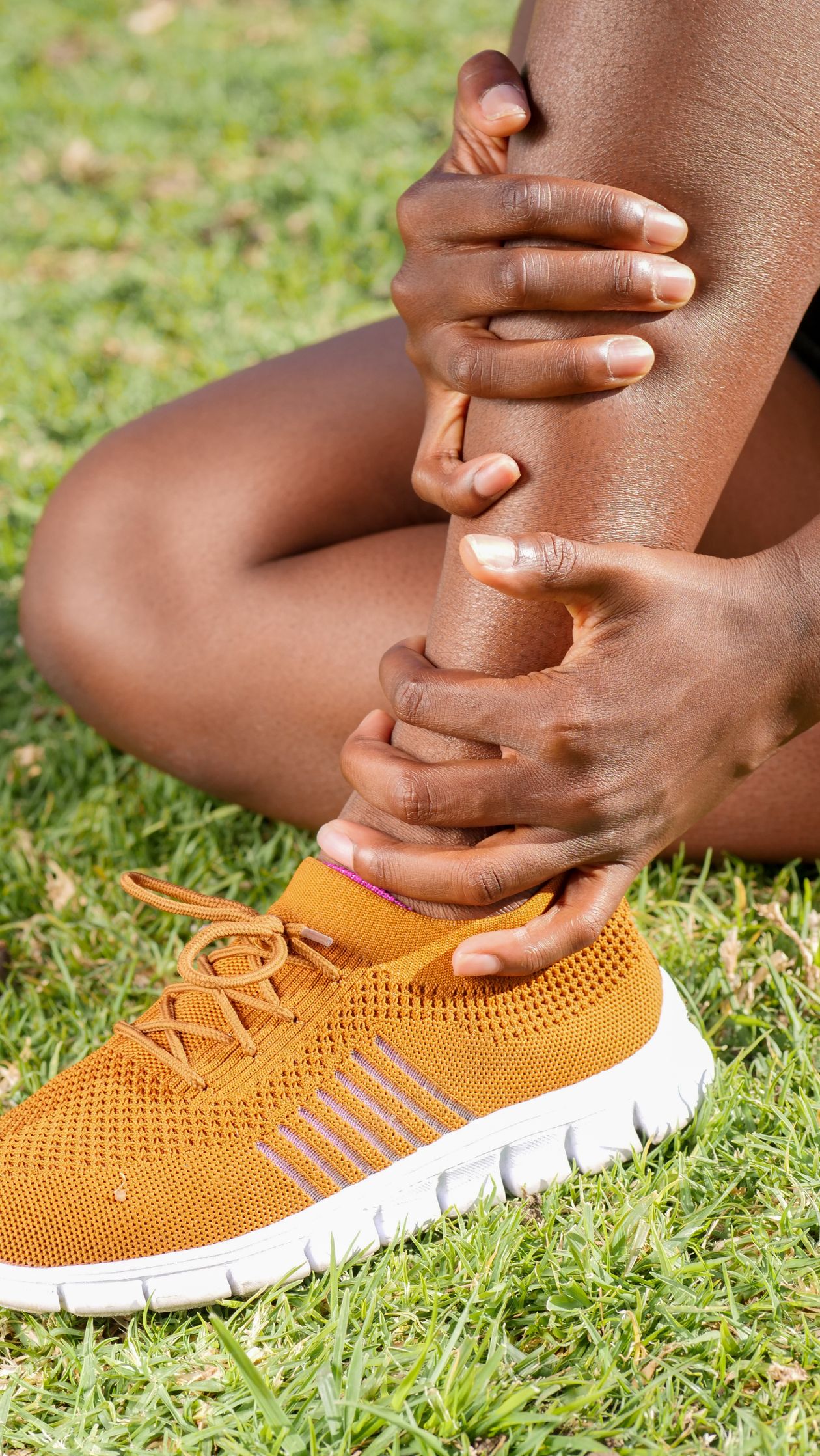 Person holding their ankle in pain sitting on grass indicating ankle injury