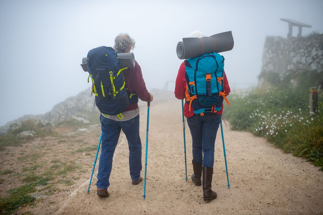 Mature couple hiking trail with walking poles demonstrating proper trekking pole technique to reduce knee stress on descents