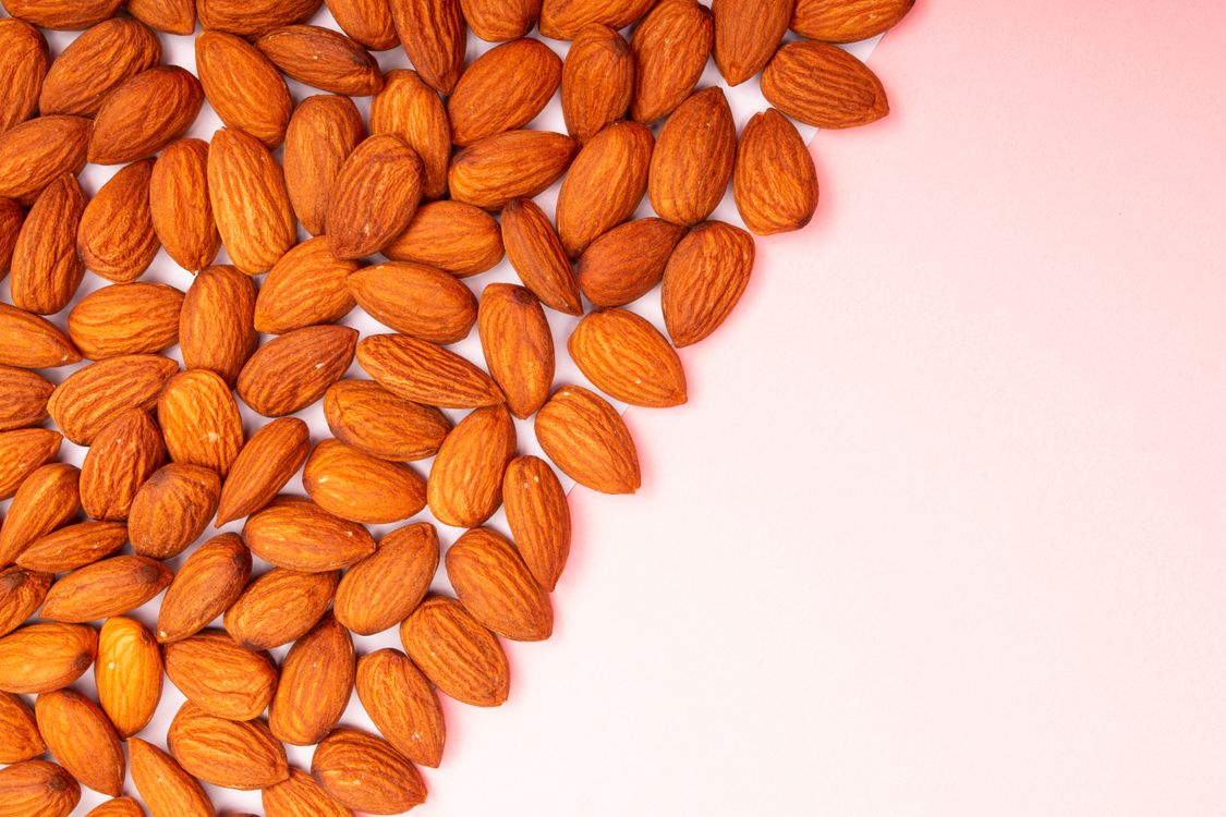 Almonds and magnesium-rich nuts on pink surface showing dietary magnesium sources for muscle recovery and joint health after 40