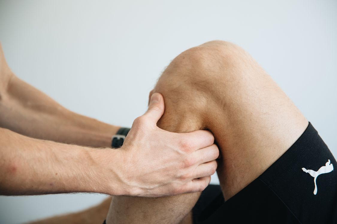 Physiotherapist treating knee joint pain with therapeutic hands-on technique showing professional rehabilitation for adults over 40