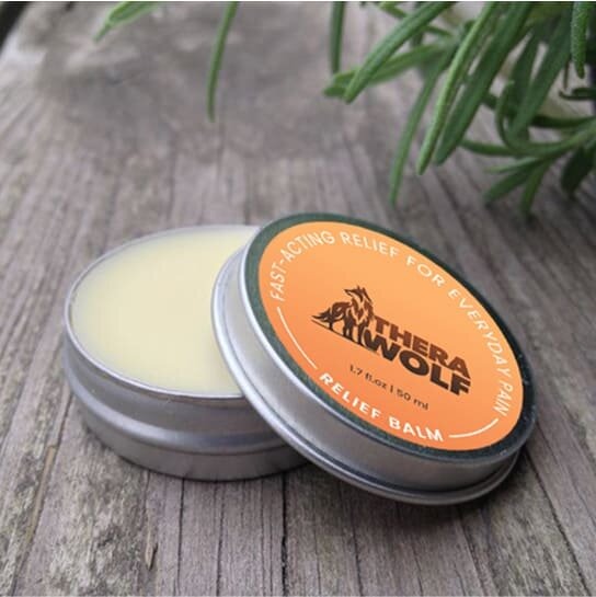 TheraWolf Pain Relief Balm tin open on wooden surface showing natural botanical balm formula with rosemary and orange label