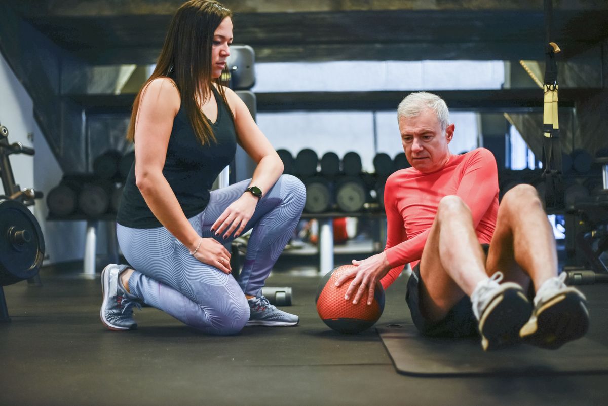 older man doing a guided shoulder exercise with a trainer to regain range of motion