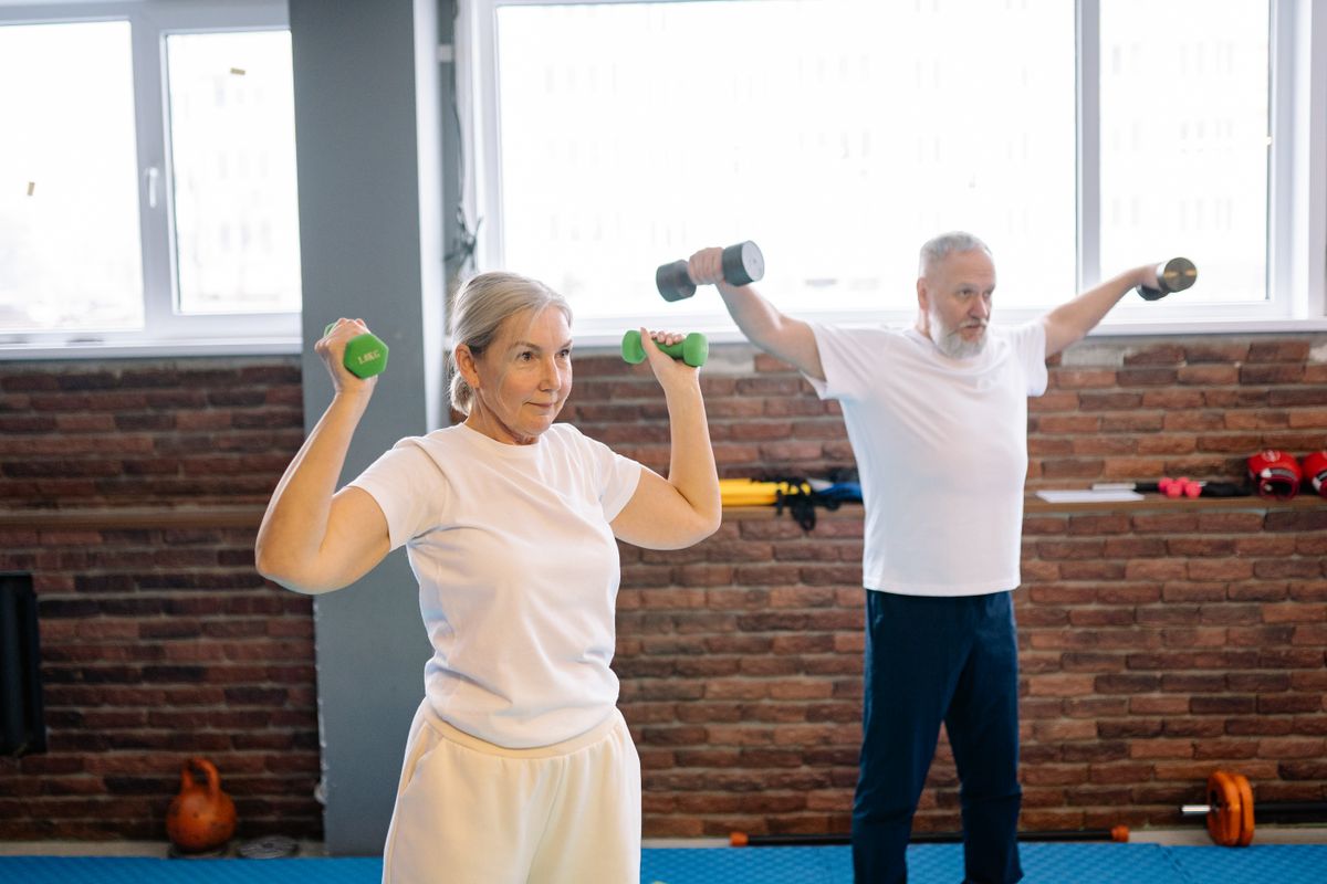 Older man and woman doing dumbbell strength training together, building grip and muscle strength for healthy aging
