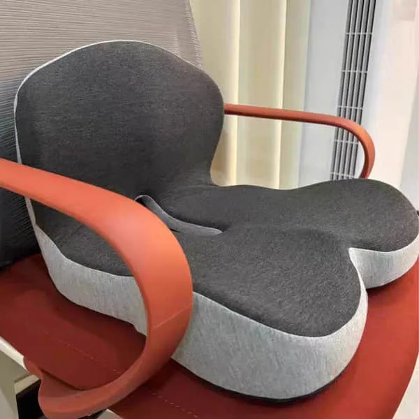 Hewelth LumboCare Pro cushion sitting on a desk chair, showing the seat with tailbone cutout and the curved back-support panel rising up behind