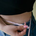 Adult measuring their waist with a tape measure as a home body composition method