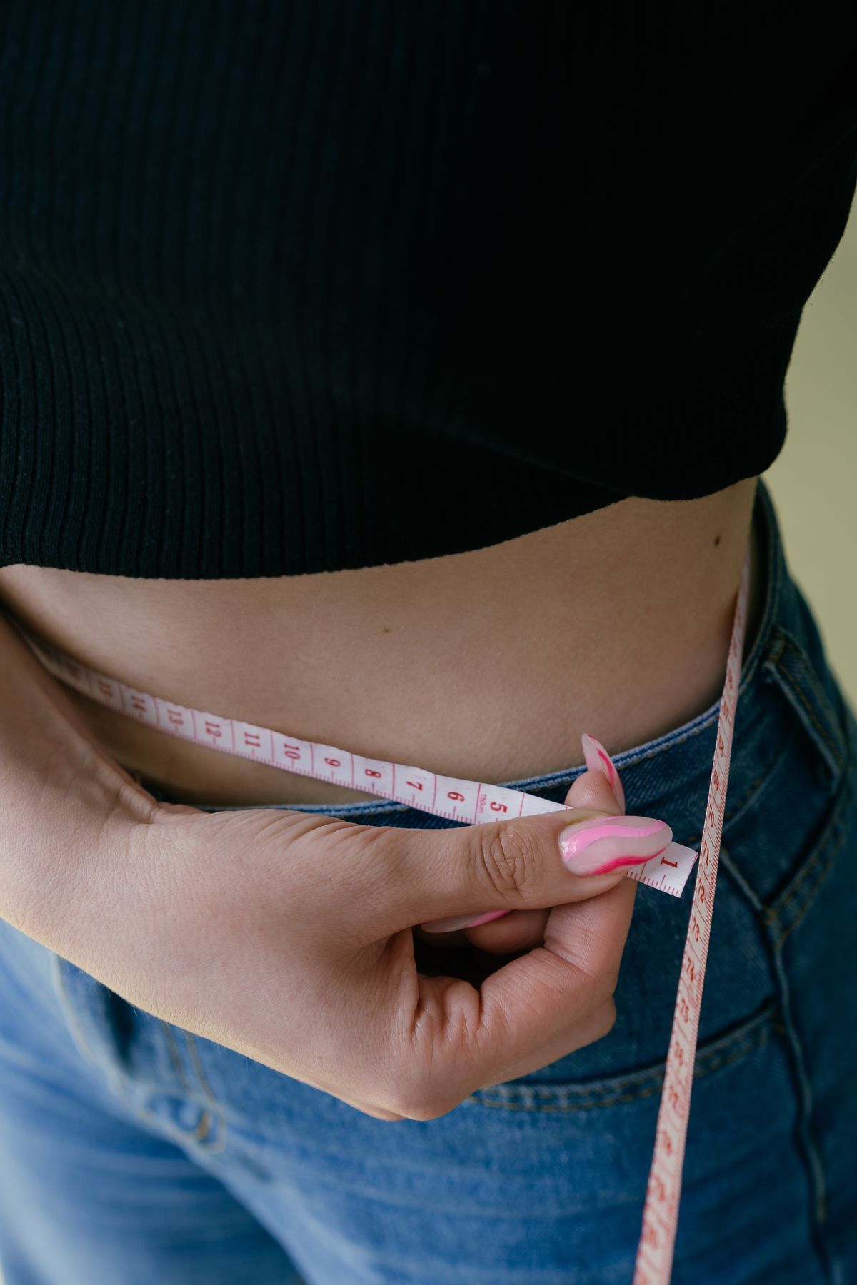 Adult measuring their waist with a tape measure as a home body composition method