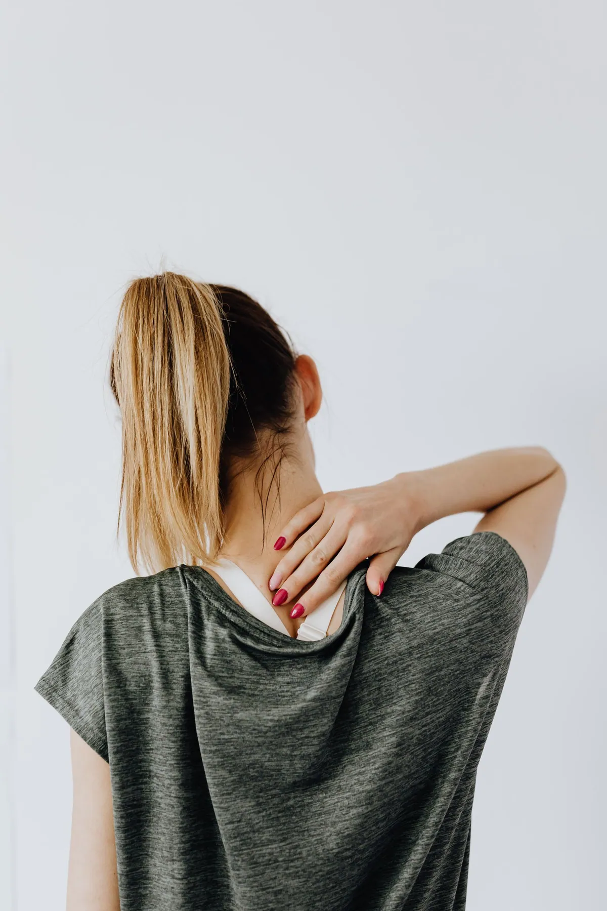 Woman holding the back of her neck with neck pain, the most common reason people shop for a butterfly pillow