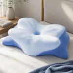 Hewelth MaxBreath butterfly pillow in white and blue memory foam with raised side wings and a central airflow hole, on a bed