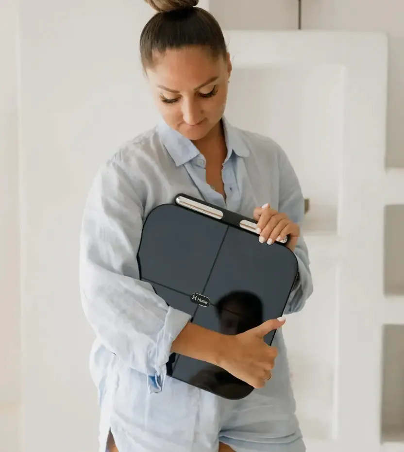 Woman holding the Hume Pod smart scale with its hand-grip handle for full-body measurement